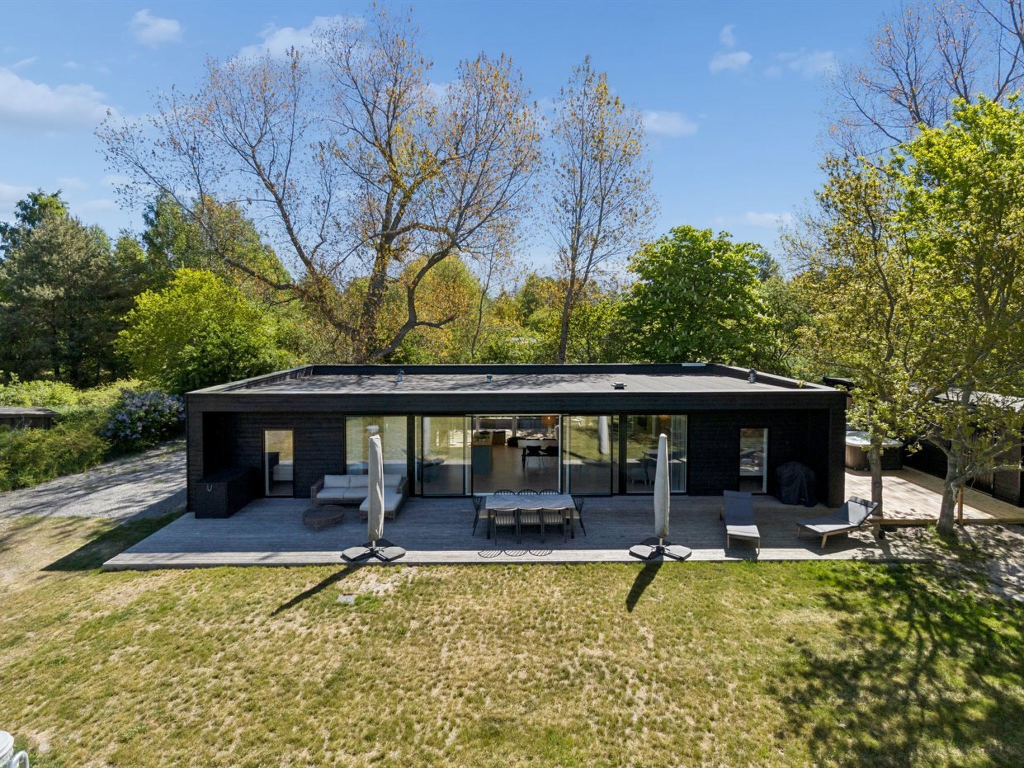 Una casa moderna con un patio, mobiliario exterior y una puerta de vidrio que da al interior.