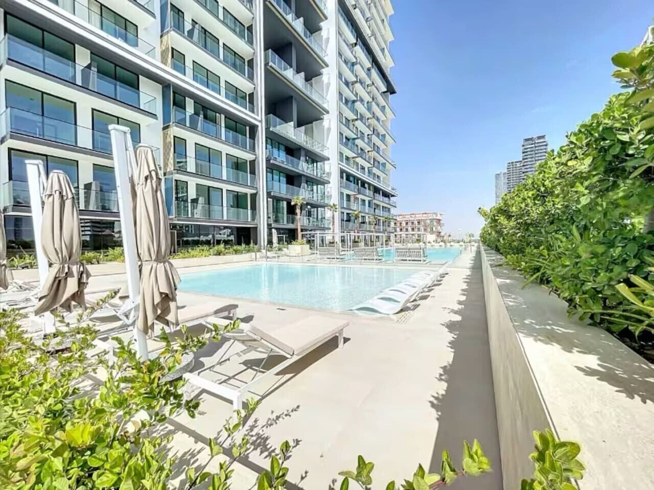A modern hotel with a swimming pool, sun loungers, and a well-maintained garden.