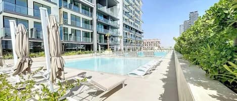 Ein modernes Hotel mit Swimmingpool, Liegestühlen und einem gepflegten Garten.