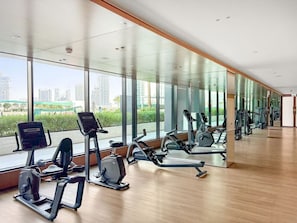 A gym with cardio machines, large windows, and a view of the cityscape. - FIRST CLASS | 1BR | Cozy Luxury Living in JVC (JVC)
