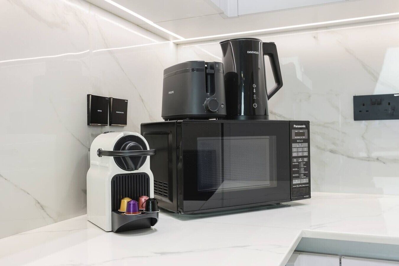 Une cuisine moderne avec un micro-ondes noir, une machine à café et un appareil blanc agrémenté de tasses colorées.