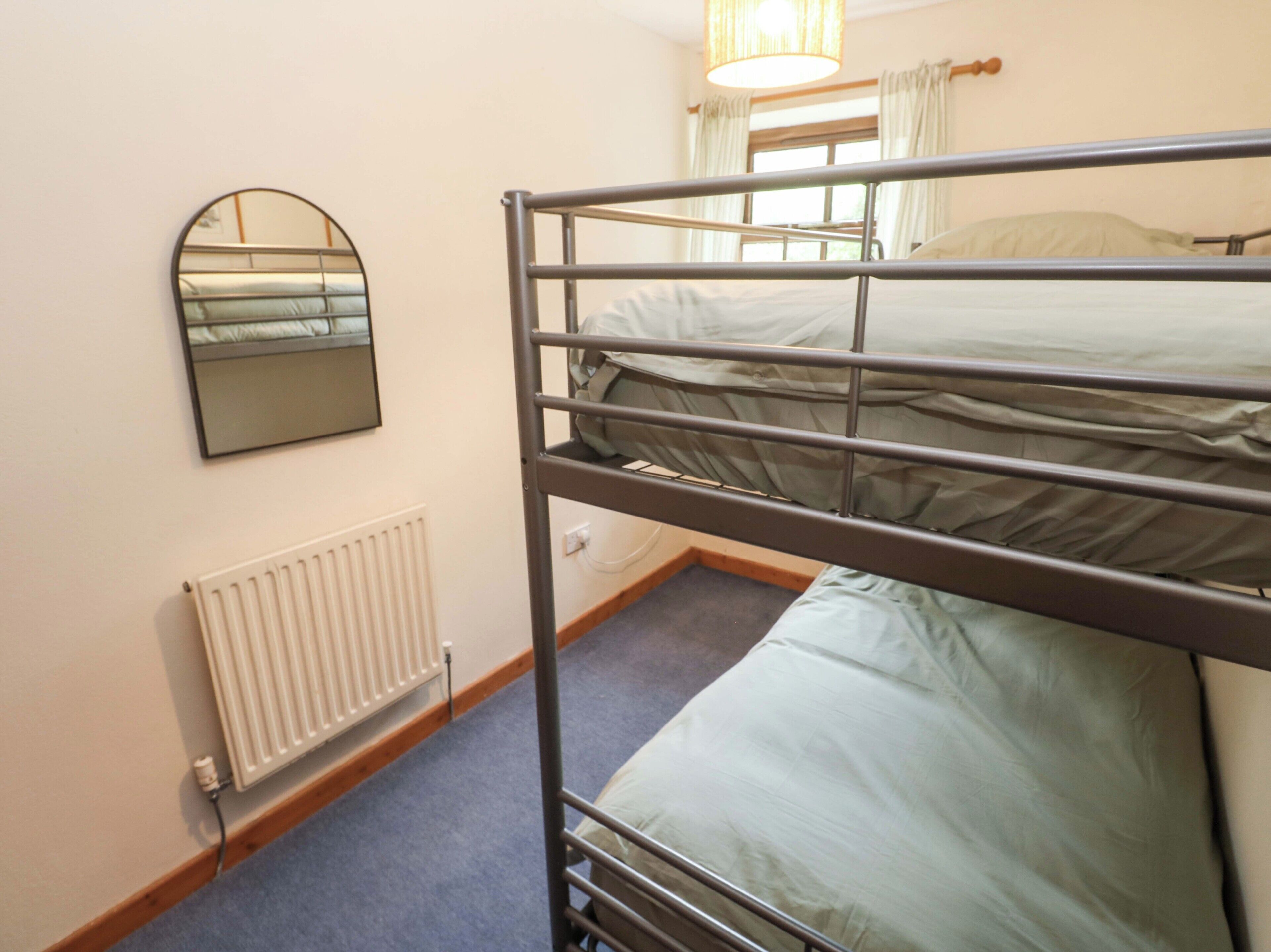 Dormitorio con literas, un radiador, un espejo y una ventana con cortinas.