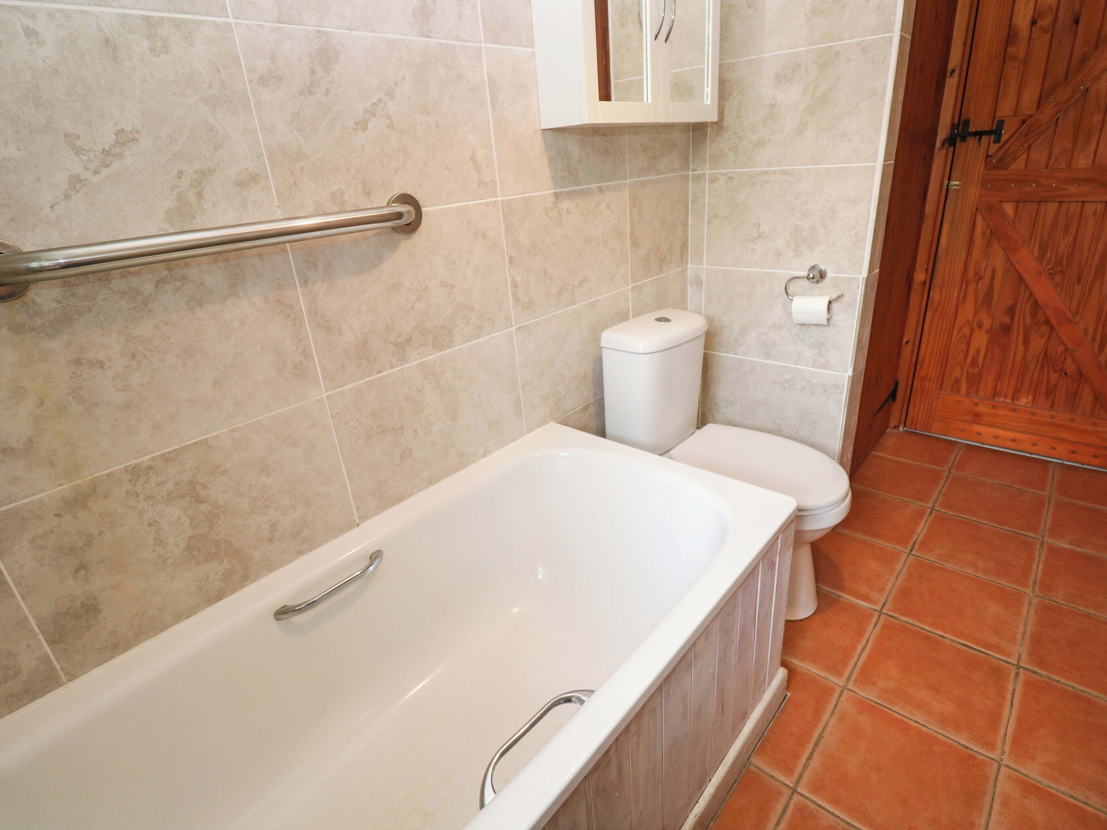 A bathroom with a bathtub, toilet, and a wooden door.