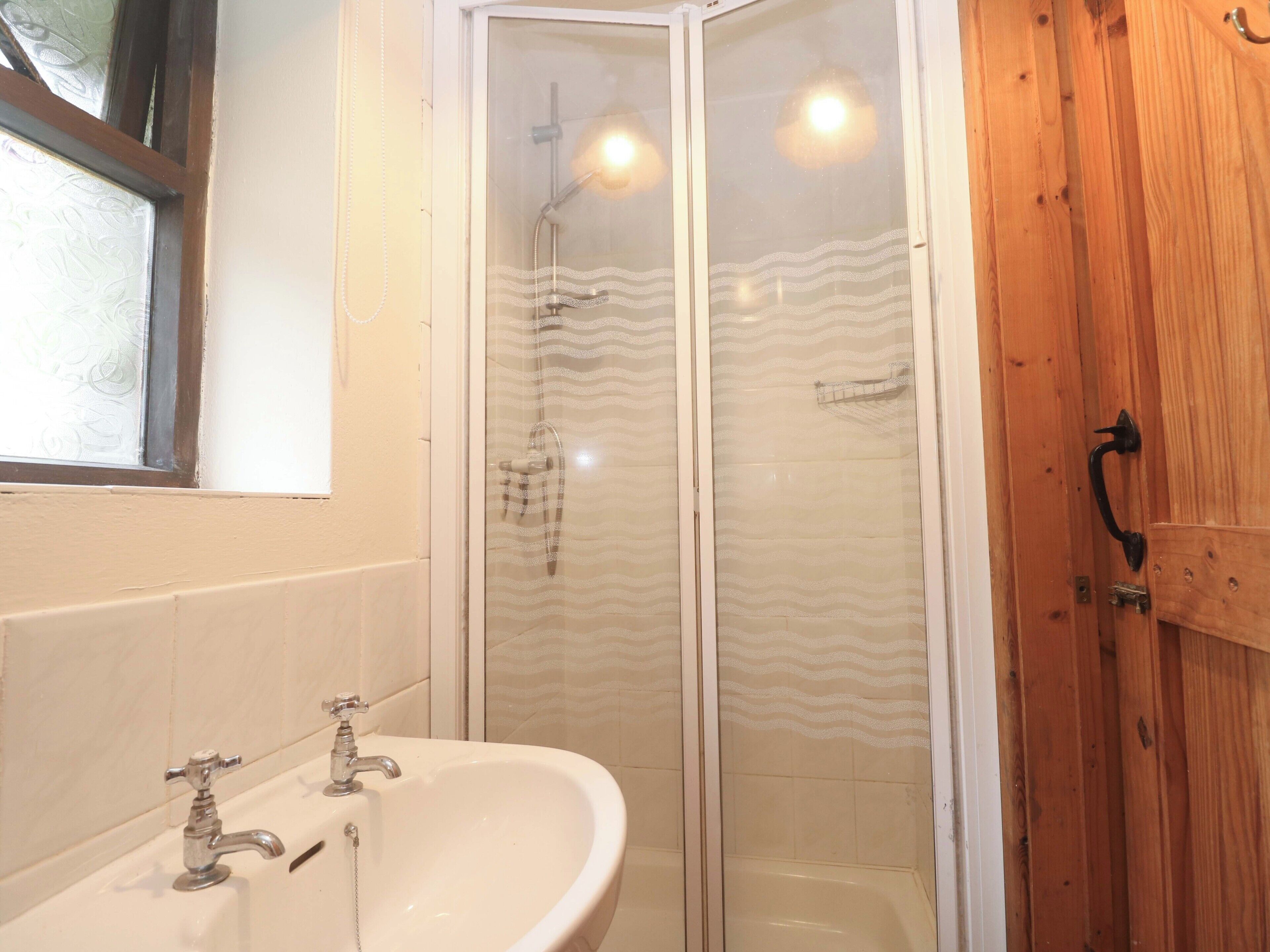 A bathroom with a white sink, a glass shower enclosure, and a wooden door.