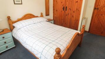 Una cama de madera con colcha a cuadros, una mesita de noche con cajones, un espejo en la pared y puertas de madera.