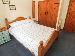 A wooden bed with a checkered bedspread, a nightstand with drawers, a mirror on the wall, and wooden doors.