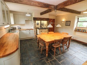 A kitchen with a wooden table, stone floor, and white cabinets.