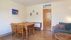Une pièce comprenant une table à manger en bois, des chaises, un canapé, un fauteuil en rotin, une porte et un radiateur.