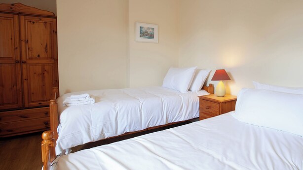 Une chambre d’hôtel avec deux lits simples, des têtes de lit en bois, une table de chevet avec une lampe et une armoire en bois.