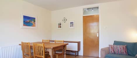 A room with a wooden dining table, chairs, a sofa, a rattan chair, a door, and a radiator.