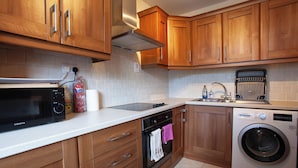 Une cuisine avec des meubles en bois, un four à micro-ondes, un grille-pain, un lave-linge et un dosseret carrelé.
