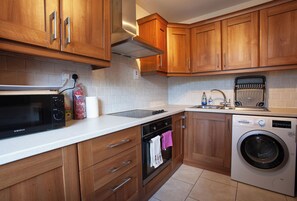 Eine Küche mit Holzschränken, einer Mikrowelle, einem Toaster, einer Waschmaschine und einer gefliesten Spritzschutzwand.