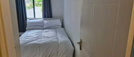 Un dormitorio con cama, ventana con cortinas, una puerta y vista a la calle.