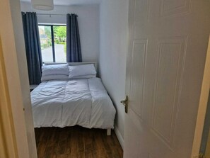 A bedroom with a bed, a window with curtains, a door, and a view of the street outside. - Spacious Bright Modern Apt With Garden (Dublin)