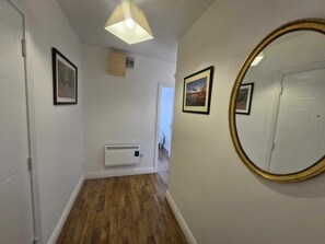 A hallway with wooden flooring, a ceiling light fixture, a wall-mounted air conditioner, and framed pictures on the walls. - Spacious Bright Modern Apt With Garden (Dublin)