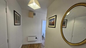 Um corredor com piso de madeira, luminária no teto, ar-condicionado fixado na parede e quadros nas paredes.