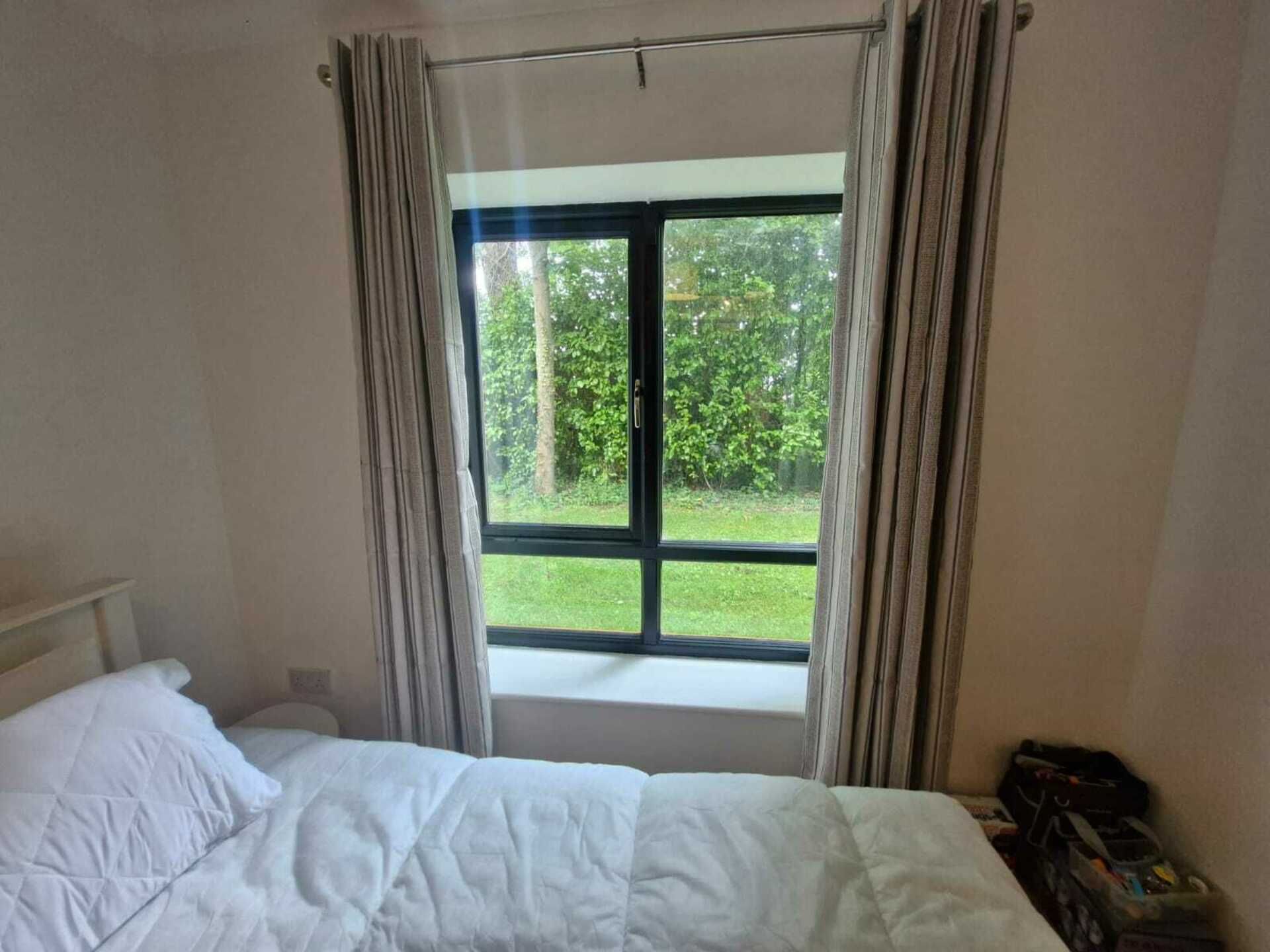 A bedroom with a bed, a window with curtains, and a view of greenery outside.
