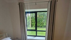 Une chambre à coucher avec un lit, une fenêtre avec des rideaux et une vue sur la verdure.
