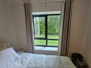 Un dormitorio con cama, ventana con cortinas y vista a zonas verdes.