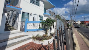 Un edificio blanco con detalles azules, una entrada con reja y una acera pavimentada.
