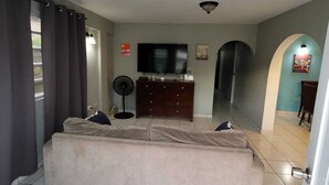 Un dormitorio con cama, cómoda, televisor y ventilador.