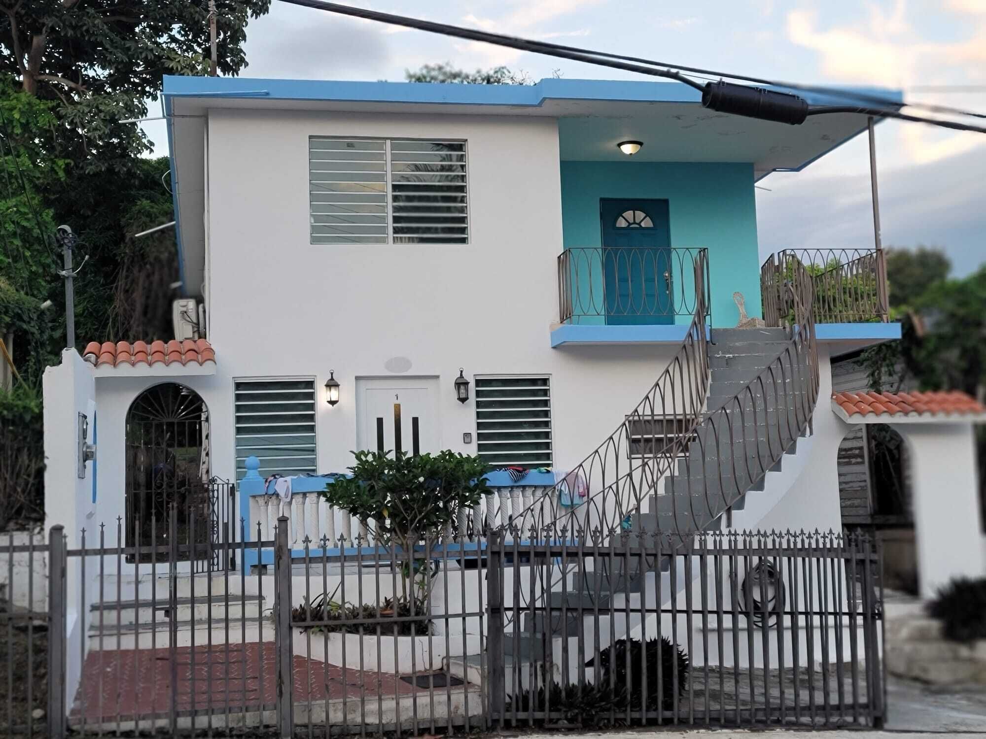 Um edifício de dois andares com fachada azul e branca, uma varanda e uma escadaria que leva ao andar superior.