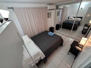 Een hotelkamer met een bed, nachtkastje, lamp en een grote spiegel die het bed en de gordijnen weerspiegelt.