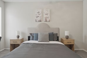 Ein Schlafzimmer mit einem Bett, zwei Nachttischen, einem Kopfteil und zwei an der Wand befestigten Bildern.