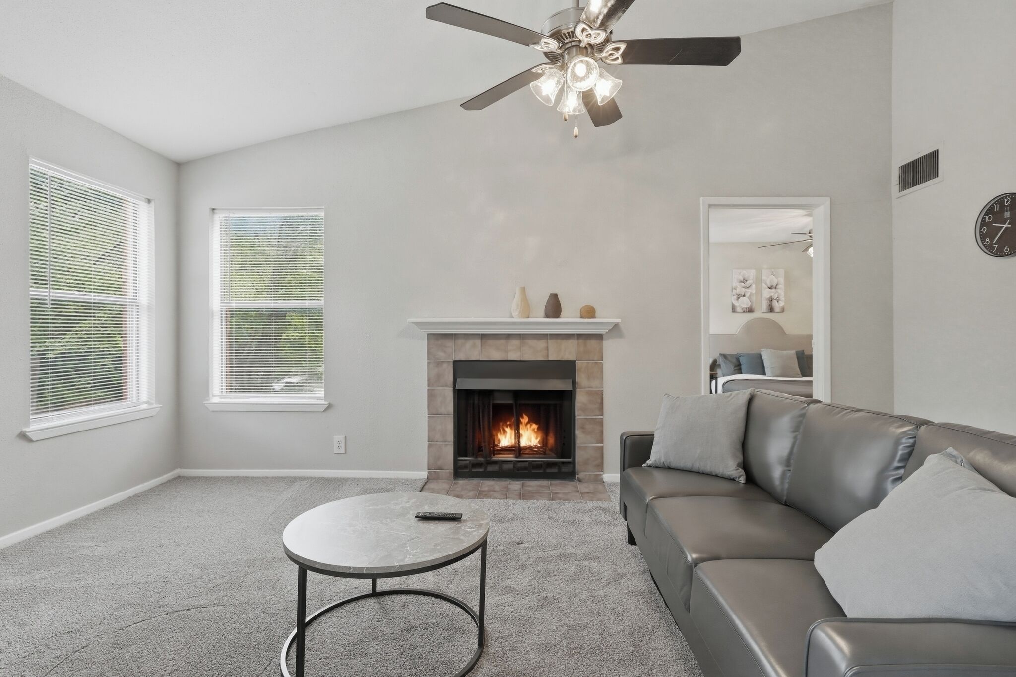 A living room with a fireplace, a sofa, a ceiling fan, and a round coffee table.