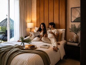 A bedroom with a bed, bedside table, lamp, and a window with curtains. - Keyrock Living | Stylish Lakeview in Business Bay (Dubai)
