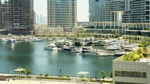 A marina with boats, a modern building with 'DAMAC' signage, and a construction site. - Keyrock Living | Stylish Lakeview in Business Bay (Dubai)