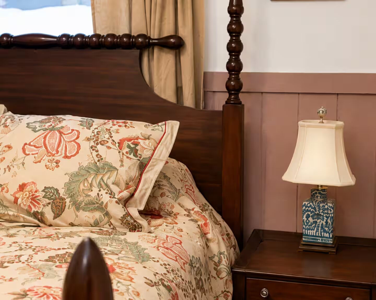 A bed with floral bedding, a wooden headboard, a nightstand with a lamp, and a dresser.