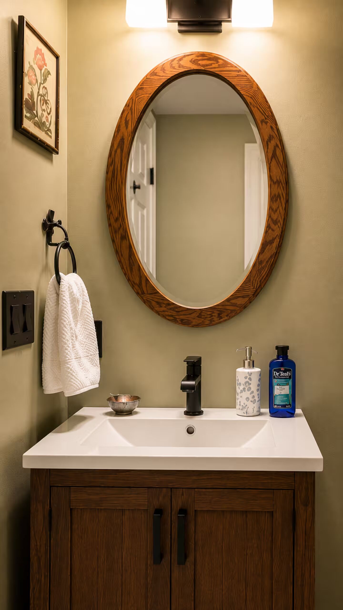 A bathroom with a wooden-framed mirror, a white sink, a towel rack, a soap dispenser, and a small bowl.