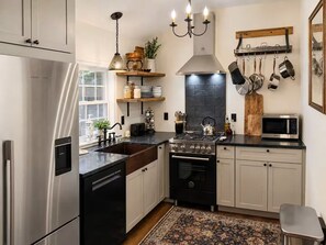 A modern kitchen with stainless steel appliances, a gas stove, a microwave, and a variety of utensils hanging on the wall. - RIVENDELL HAVEN (Glen)
