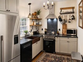 Una cocina moderna con electrodomésticos de acero inoxidable, una estufa a gas, un microondas y una variedad de utensilios colgados en la pared.