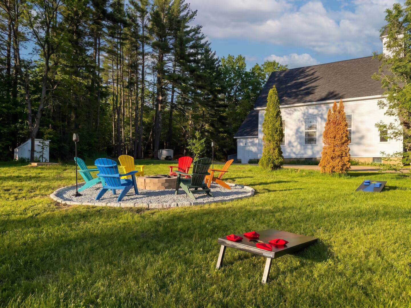 Un patio trasero con una fogata, sillas Adirondack y una pequeña mesa con servilletas rojas.