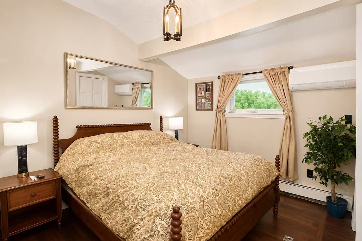 Un dormitorio con una cama grande, una mesita de noche, un espejo, una ventana con cortinas y una planta en maceta.