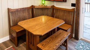 Una mesa de madera para comer con bancos, un cuadro enmarcado, una chimenea y un televisor.
