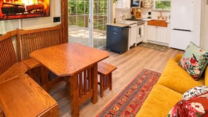 Una sala de estar acogedora con una mesa de comedor de madera, un sofá y una cocina con armarios blancos y un ventanal grande.