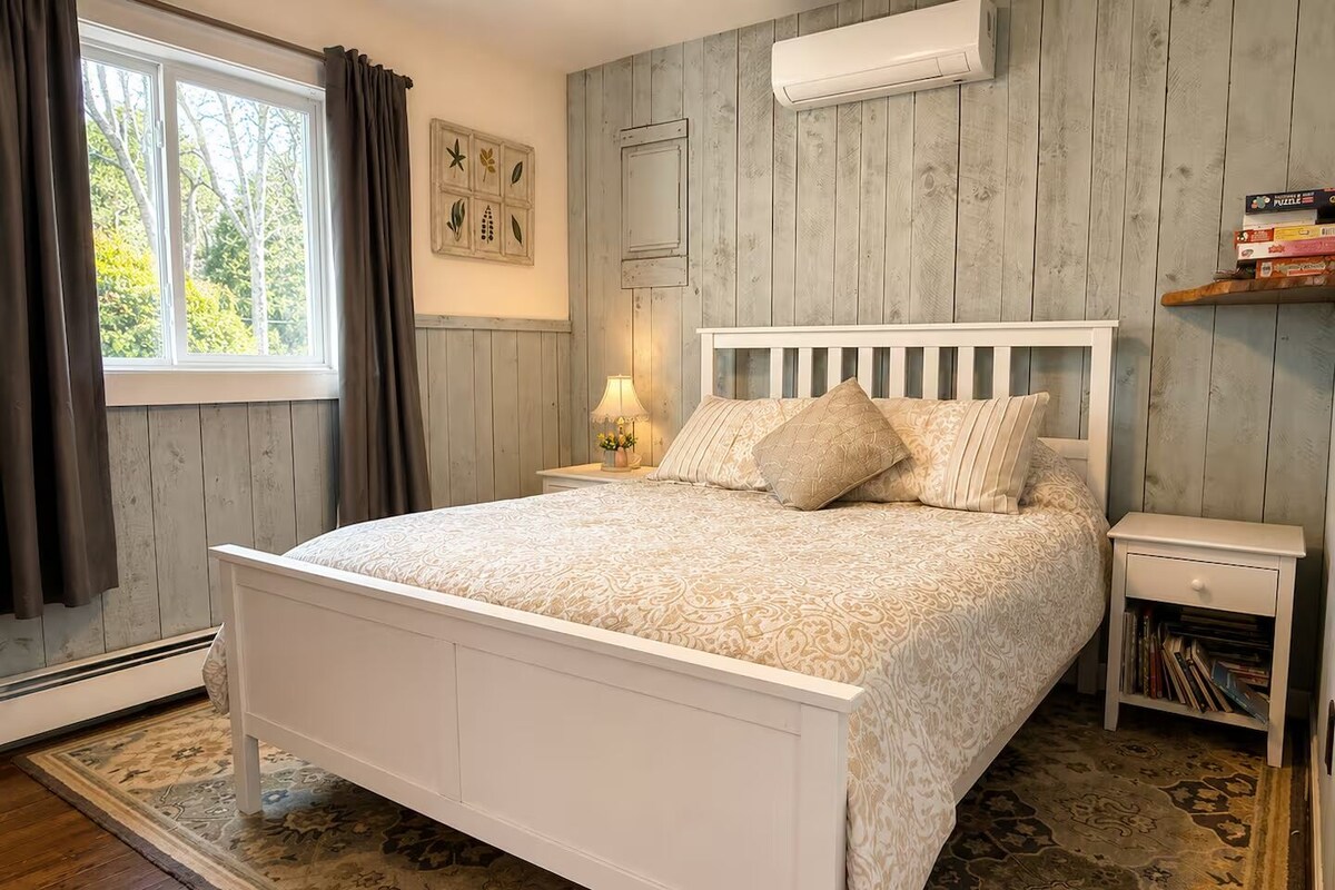 A bedroom with a bed, nightstand, bedside table, and a window with curtains.
