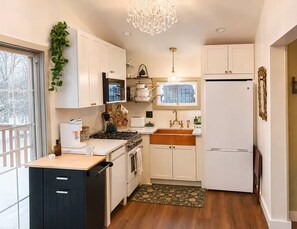 A compact kitchen with white cabinets, a stove, a sink, and a refrigerator.
