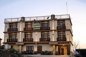 Un hotel de varios pisos con balcones, un cartel que dice 'HOTEL DIWAN SACHPASS' y varias motocicletas estacionadas en la entrada.