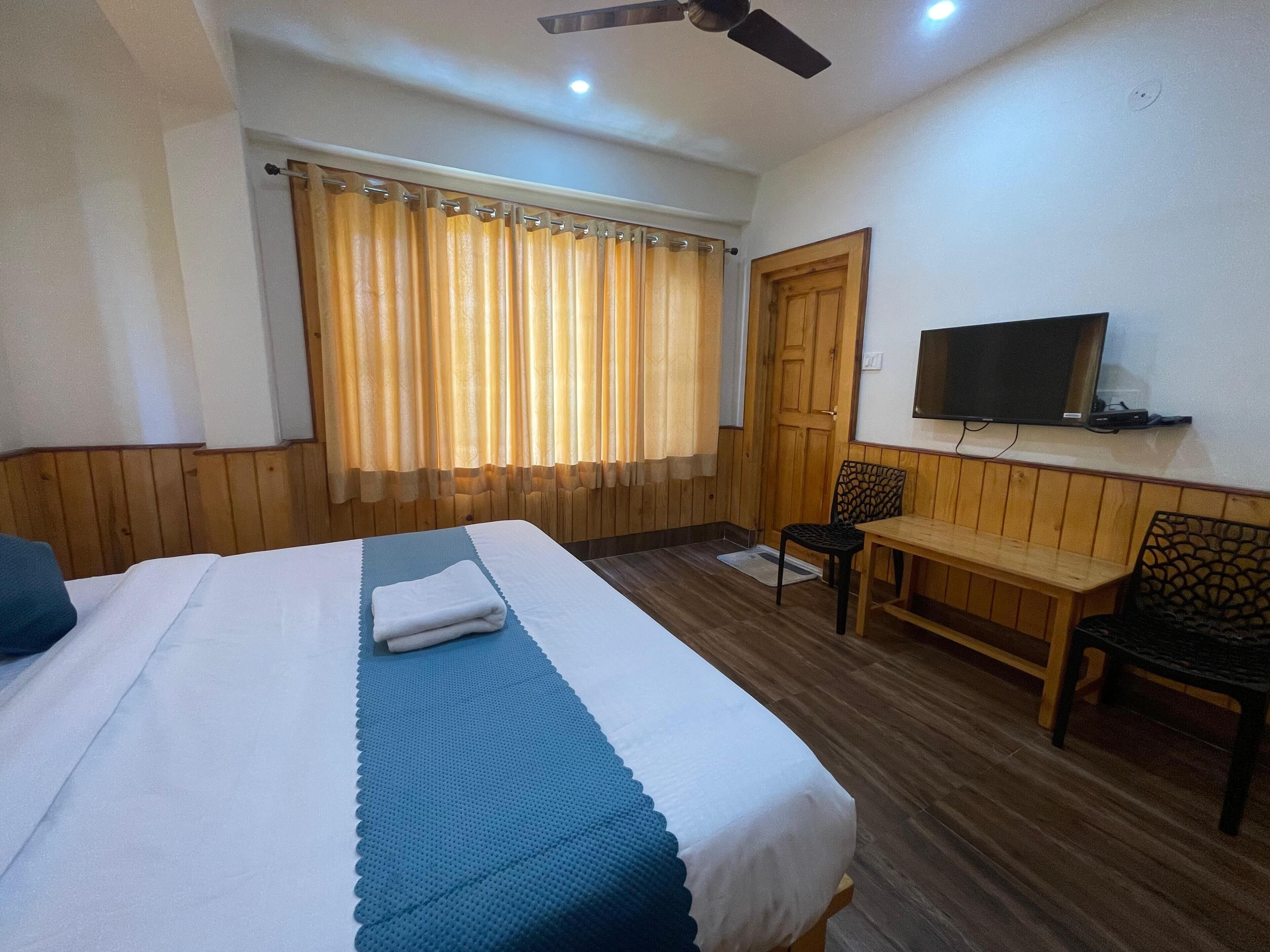 A hotel room with a bed, a desk, a chair, a television, and a window with curtains.