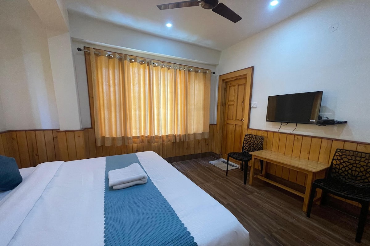 A hotel room with a bed, a desk, a chair, a television, and a window with curtains.