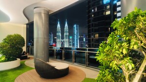 Ein moderner Balkon mit Blick auf die Petronas Towers, einem runden Sitzbereich und üppigem Grün.