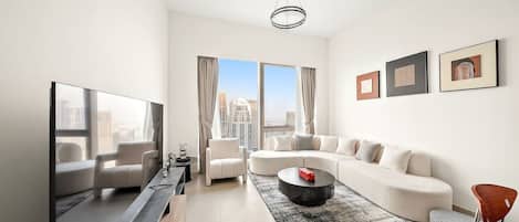 A modern living room with a large flat-screen TV, a sectional sofa, a round coffee table, and a city view through large windows.