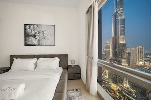 A bedroom with a large bed, a nightstand, a framed picture, and a view of a cityscape. - FIRST CLASS | 1BR | Burj Khalifa & Fountain View (Downtown)