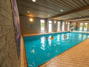Ein Hallenbad mit gefliesten Wänden, Holzbalken an der Decke und einem Fliesenboden.