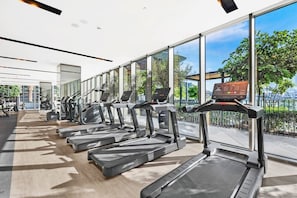 Ein Fitnessstudio mit Laufbändern, Trainingsgeräten und großen Fenstern mit Blick ins Freie.