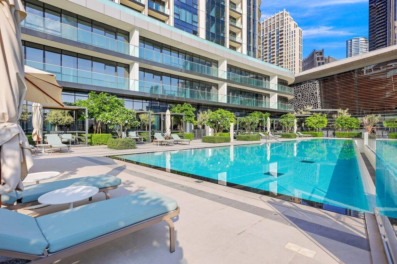 Um hotel moderno com piscina no terraço, espreguiçadeiras e fachada de vidro.